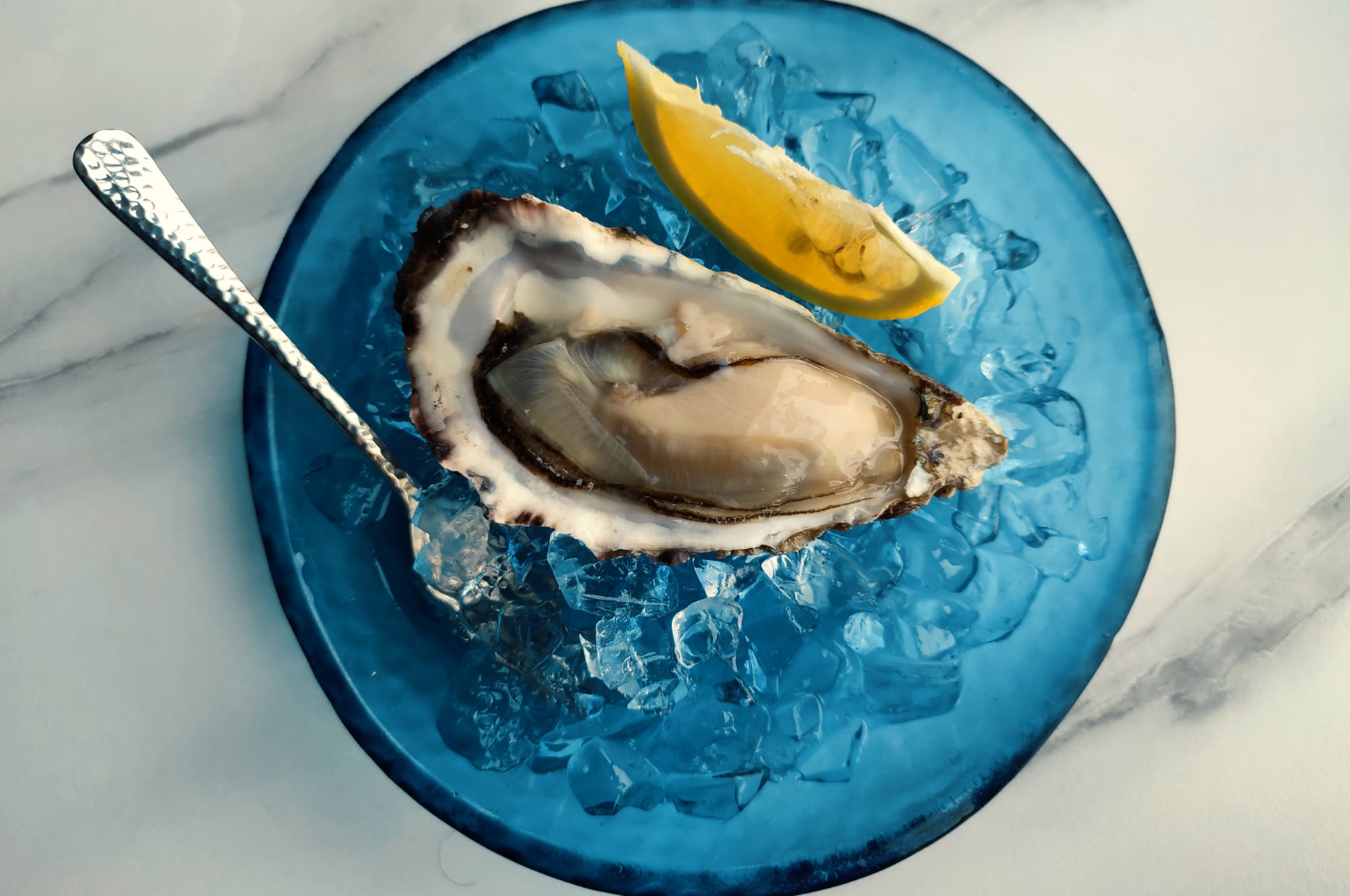 Oyster plated with lemon on a blue saucer, with a spoon
